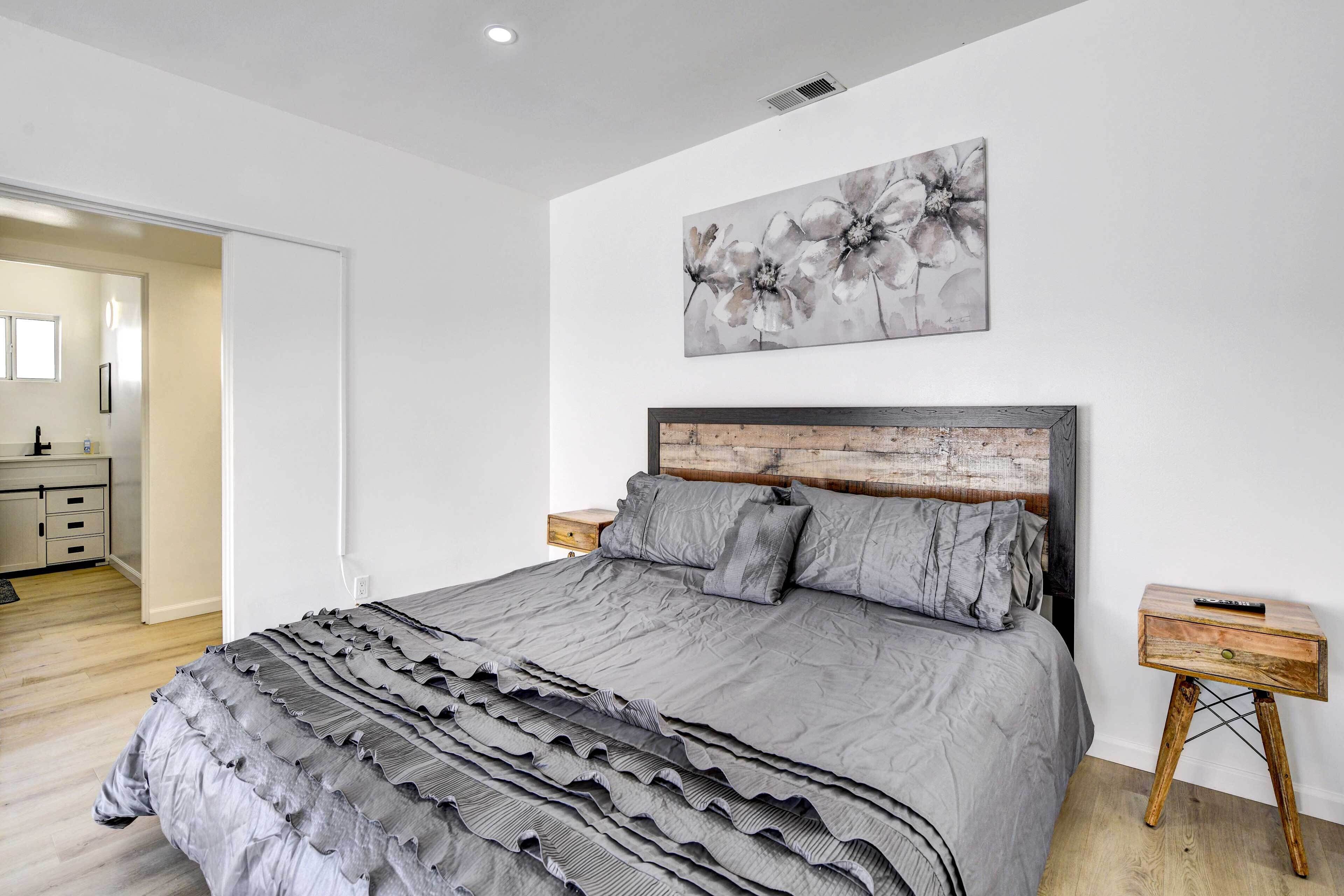 A bedroom with a large bed, a wooden headboard, a nightstand, and a painting on the wall.