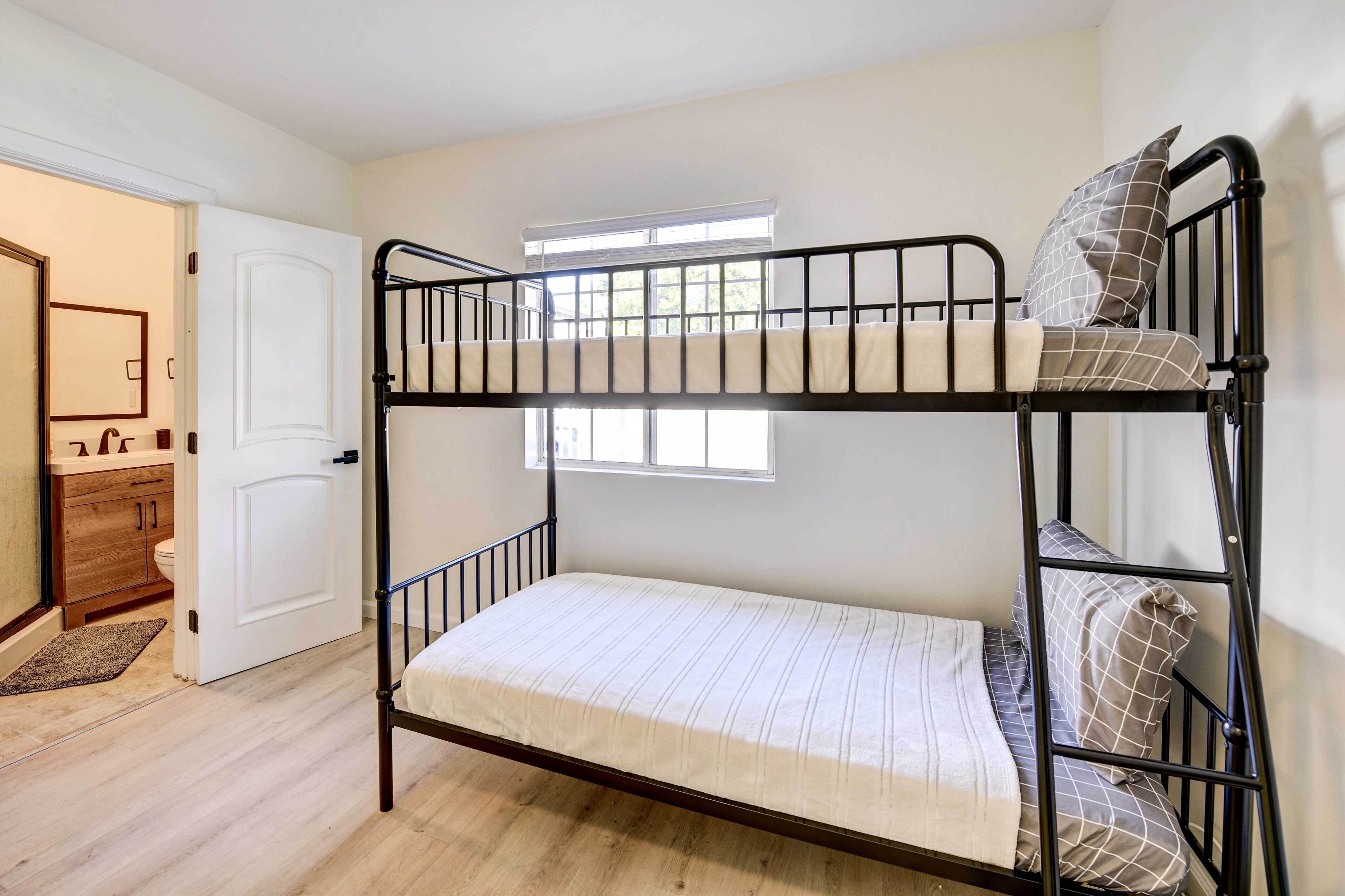 A bunk bed with a mattress and pillows, a door, a window, and a bathroom with a sink and mirror.