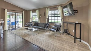Un salón amplio con suelo de madera oscura, un sofá modular grande, dos sillones, una mesa de centro y un televisor de pantalla plana montado en la pared.