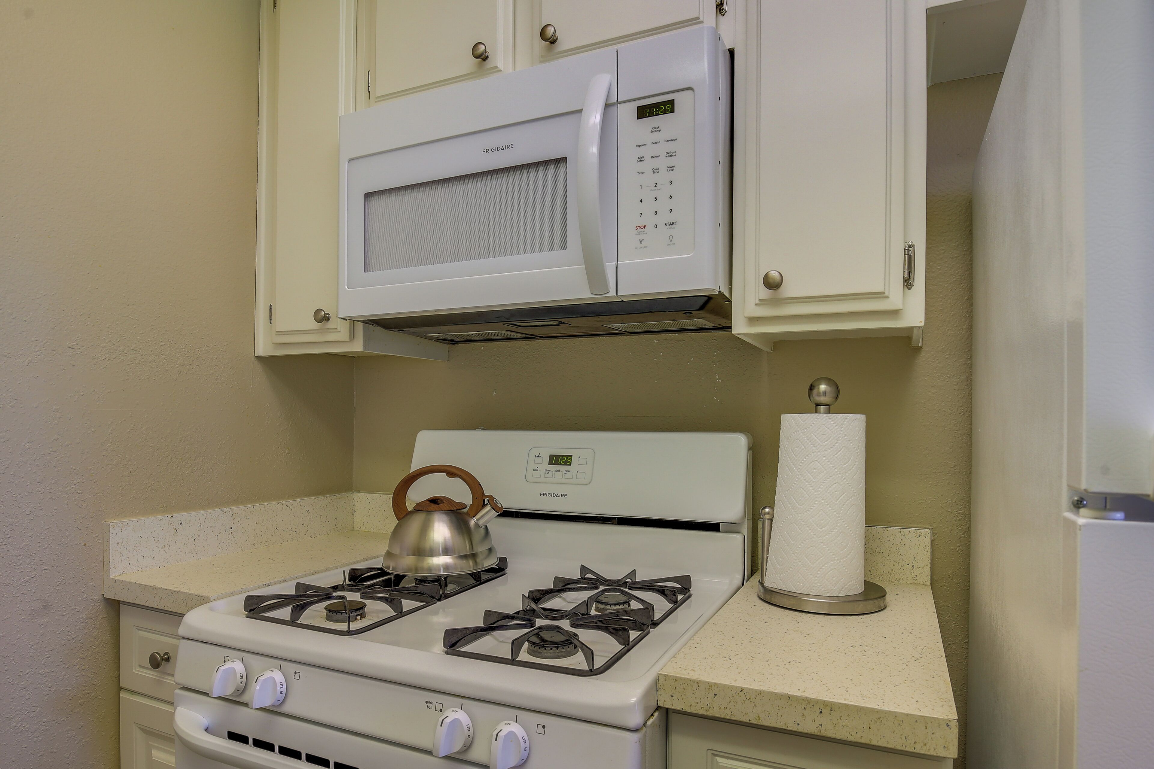 A kitchen with a white stove, a kettle, a microwave, and a roll of paper towels.