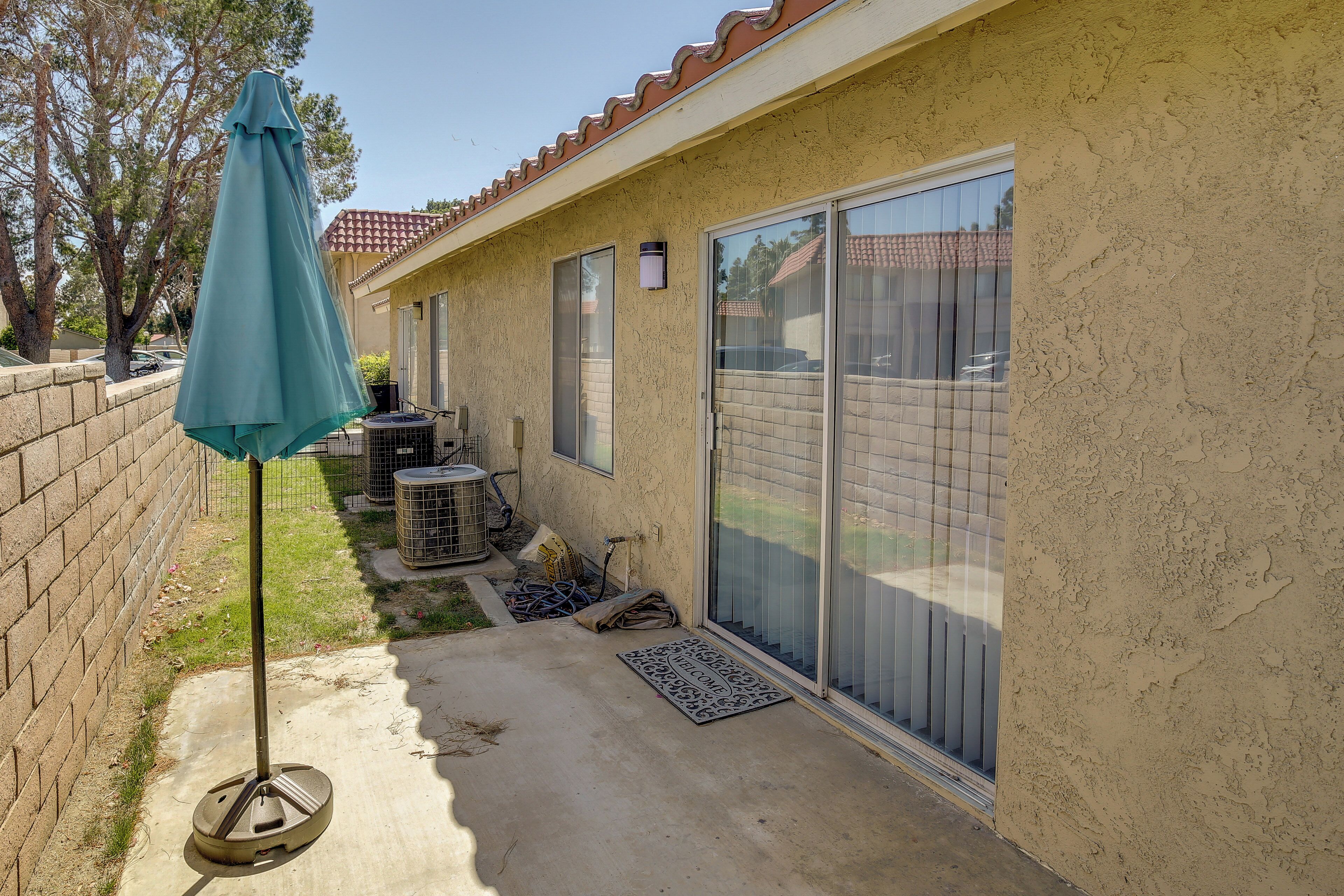 A patio area with a concrete floor, a green umbrella, a metal grill, and a sliding glass door.