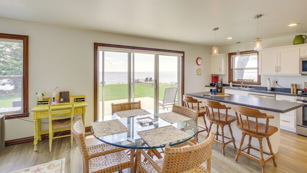 A modern kitchen with a large island, dining area with wicker chairs, and a view of the outdoors. - La Petit Maison - Lakefront Oshkosh Home! (Oshkosh)
