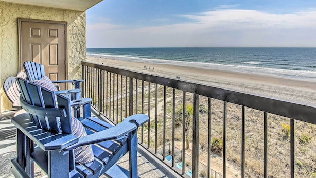 Ein Balkon mit Blick auf den Strand, ausgestattet mit Adirondack-Stühlen und einer Tür.