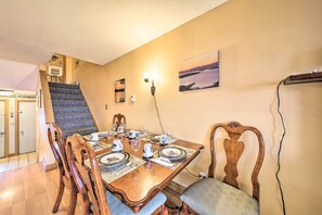A dining area with a wooden table set for four, a staircase, and a wall-mounted light fixture. - Condo w/ Rangeley Lake Views: 10 Mi to Saddleback! (Rangeley)