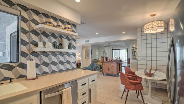 A modern kitchen with a central island, white cabinetry, and a dining area with a round table and orange chairs. - Chic Palm Springs Gem w/ Patio + Pool Access! (Palm Springs)