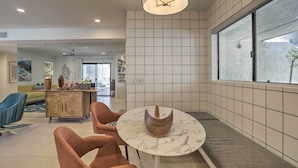 A modern living room with a round marble table, two cushioned chairs, a wooden cabinet, and a large window with a view. - Chic Palm Springs Gem w/ Patio + Pool Access! (Palm Springs)
