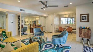 A modern living room with a glass coffee table, blue armchairs, a yellow sofa, and a dining area with orange chairs. - Chic Palm Springs Gem w/ Patio + Pool Access! (Palm Springs)
