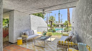 A patio area with a sofa, coffee table, and yellow chairs. There is a pool visible in the background. - Chic Palm Springs Gem w/ Patio + Pool Access! (Palm Springs)