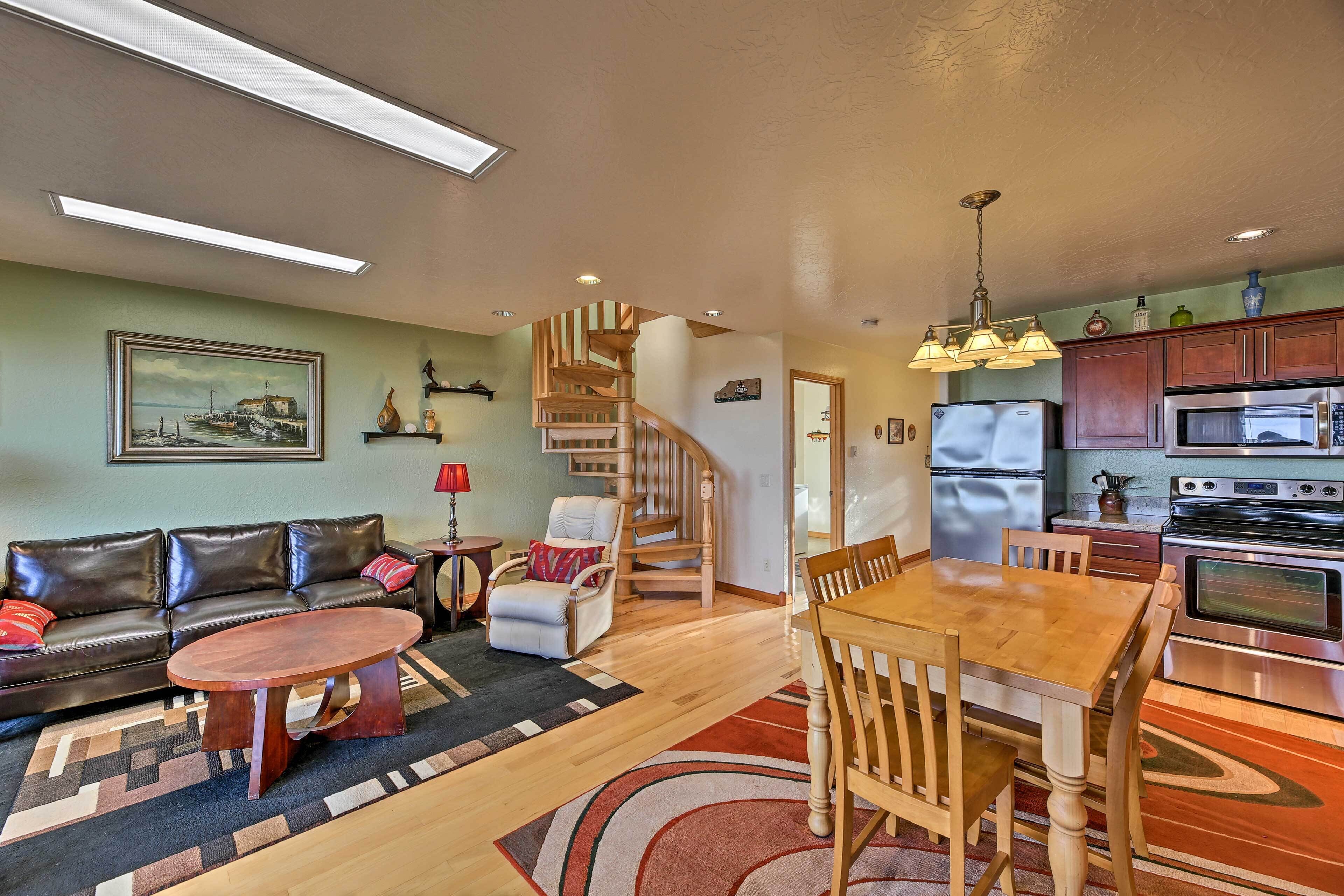 A living room with a sofa, coffee table, and a dining area with a wooden table and chairs. There is a staircase leading to another level.