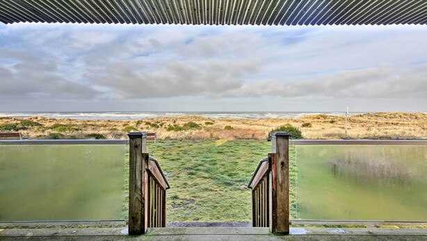 Vista de um espaço coberto com telhado de metal, com acesso a um campo gramado e um corpo d'água.