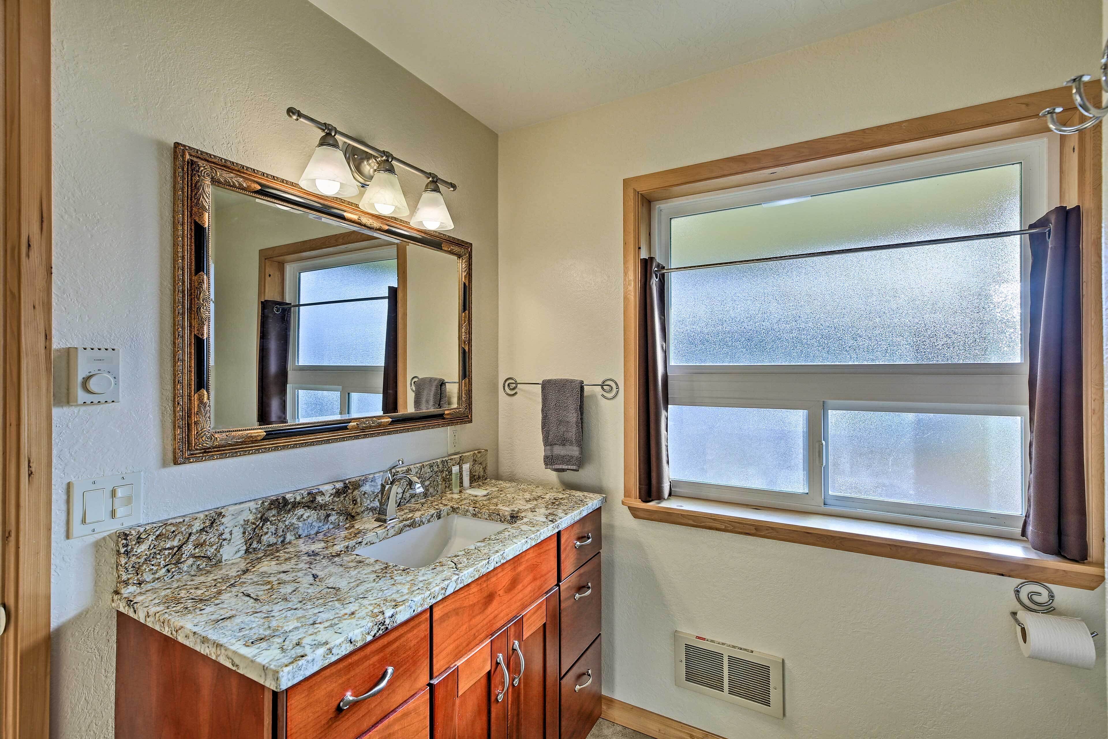 A bathroom with a marble sink, wooden vanity, a large mirror, and a window with curtains.