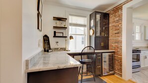 A kitchen with a marble countertop, a wooden chair, a brick wall, and a built-in oven. - Beautiful Colonial Home on the Choptank River (Cambridge)