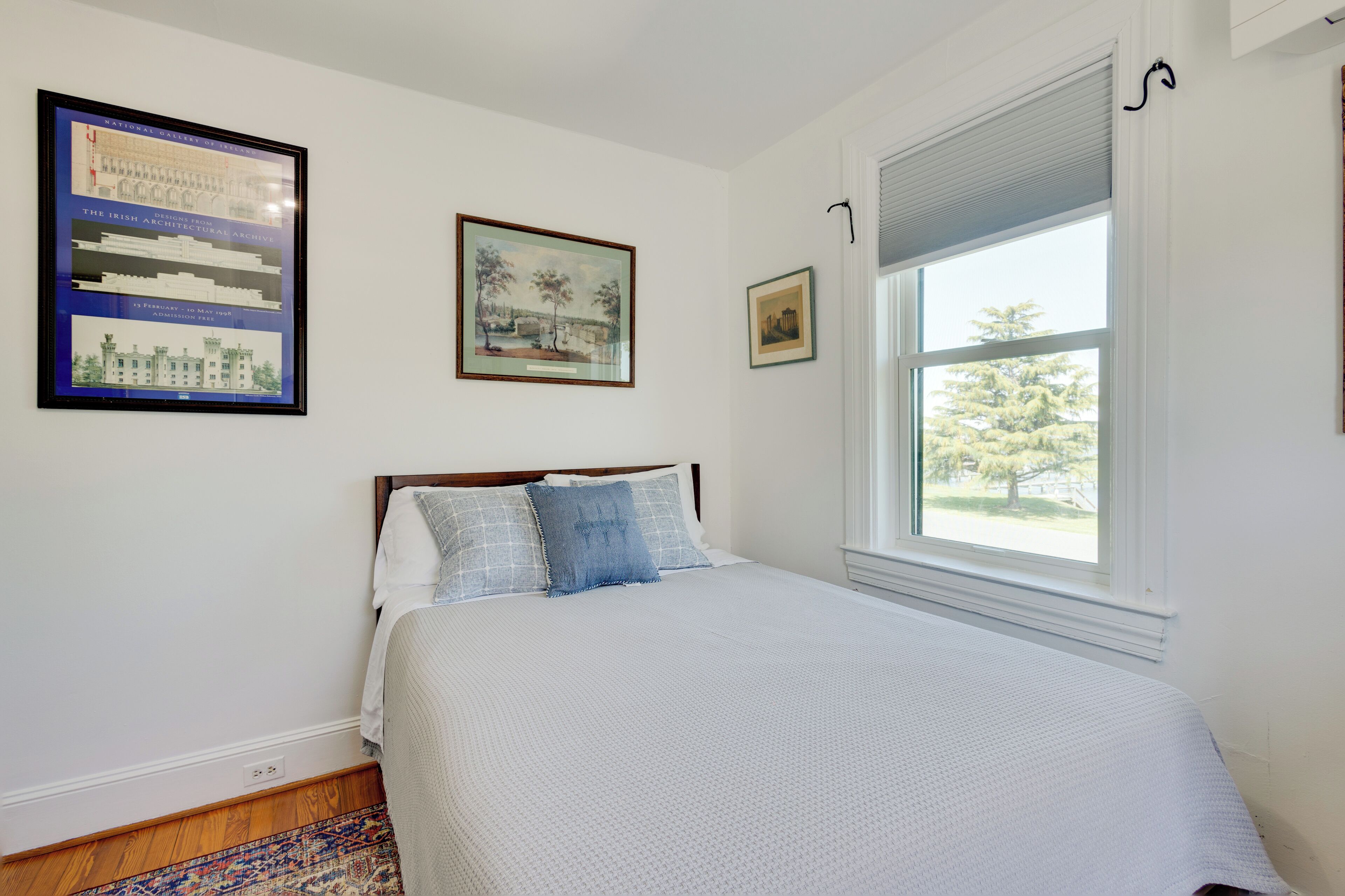 A bedroom with a bed, a window with blinds, and framed pictures on the wall.