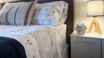 A neatly made bed with a white duvet and pillows featuring a pattern of crosses and oars. A wooden bedside table with a lamp and a decorative object is visible.