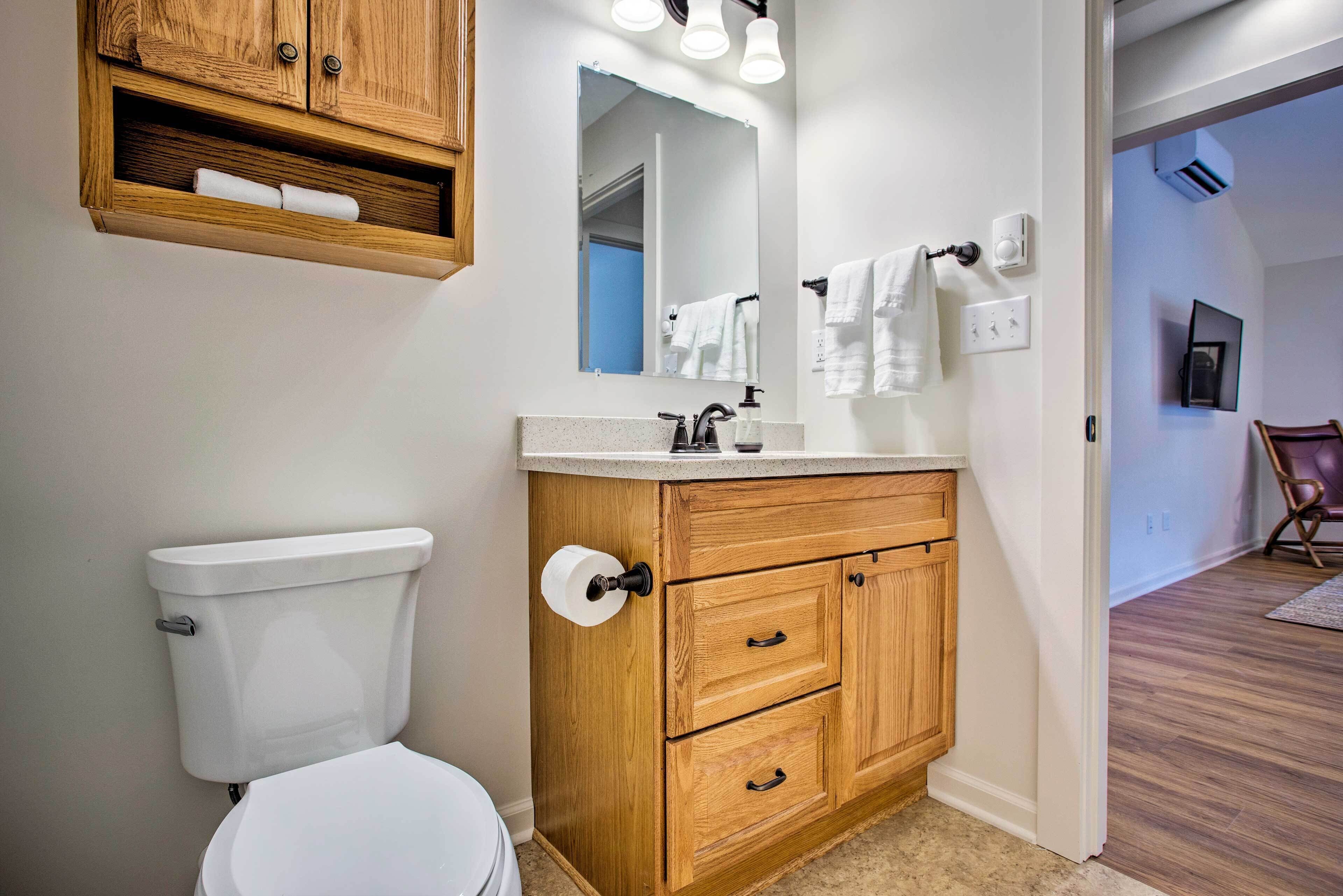 A bathroom with a wooden vanity, a toilet, a mirror, and a towel rack.