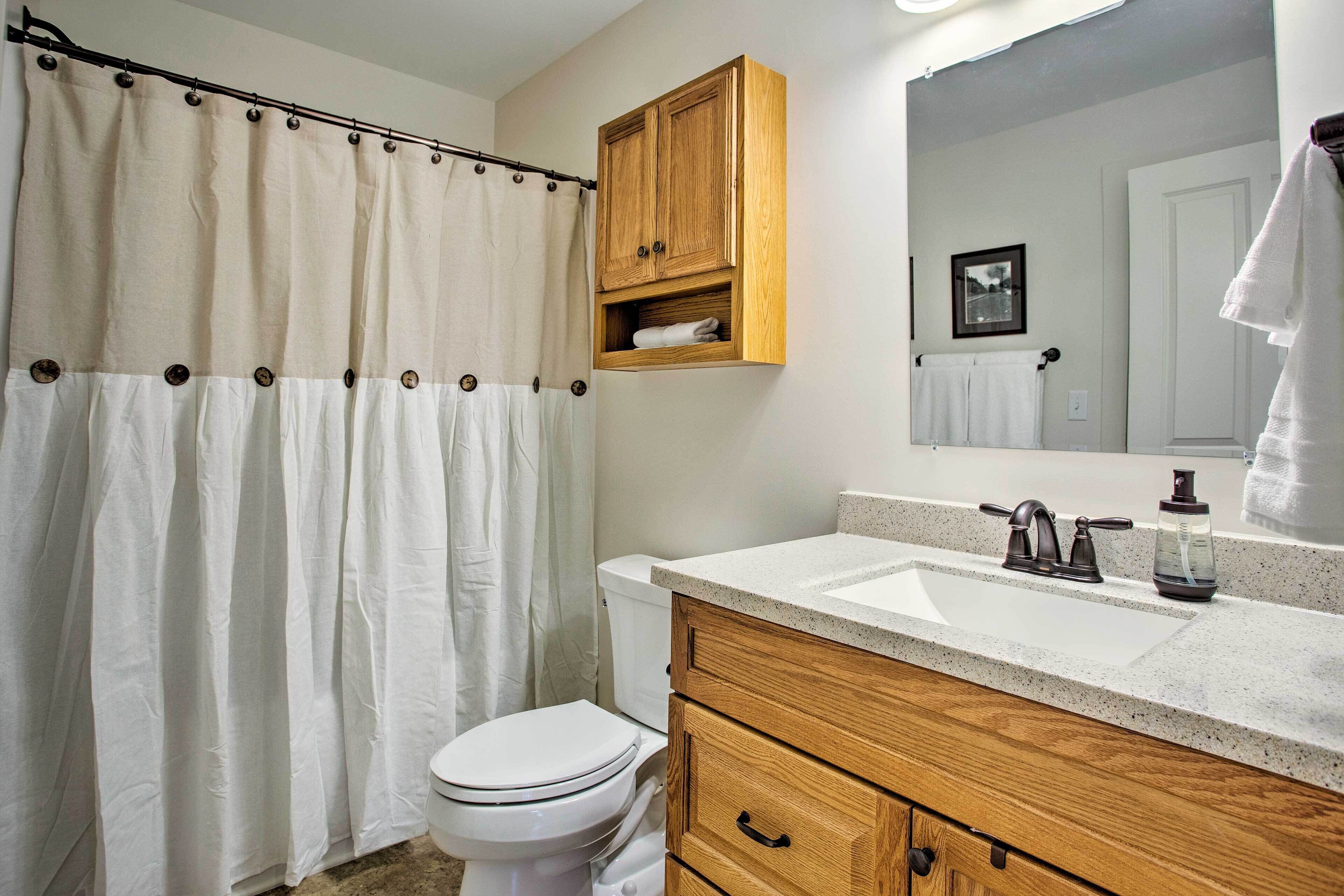 A bathroom with a shower curtain, toilet, wooden cabinet, and a sink with a mirror above it.