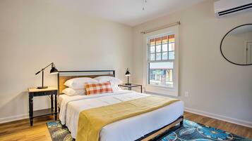 A bedroom with a bed, a nightstand, a lamp, a window with blinds, and a patterned rug.