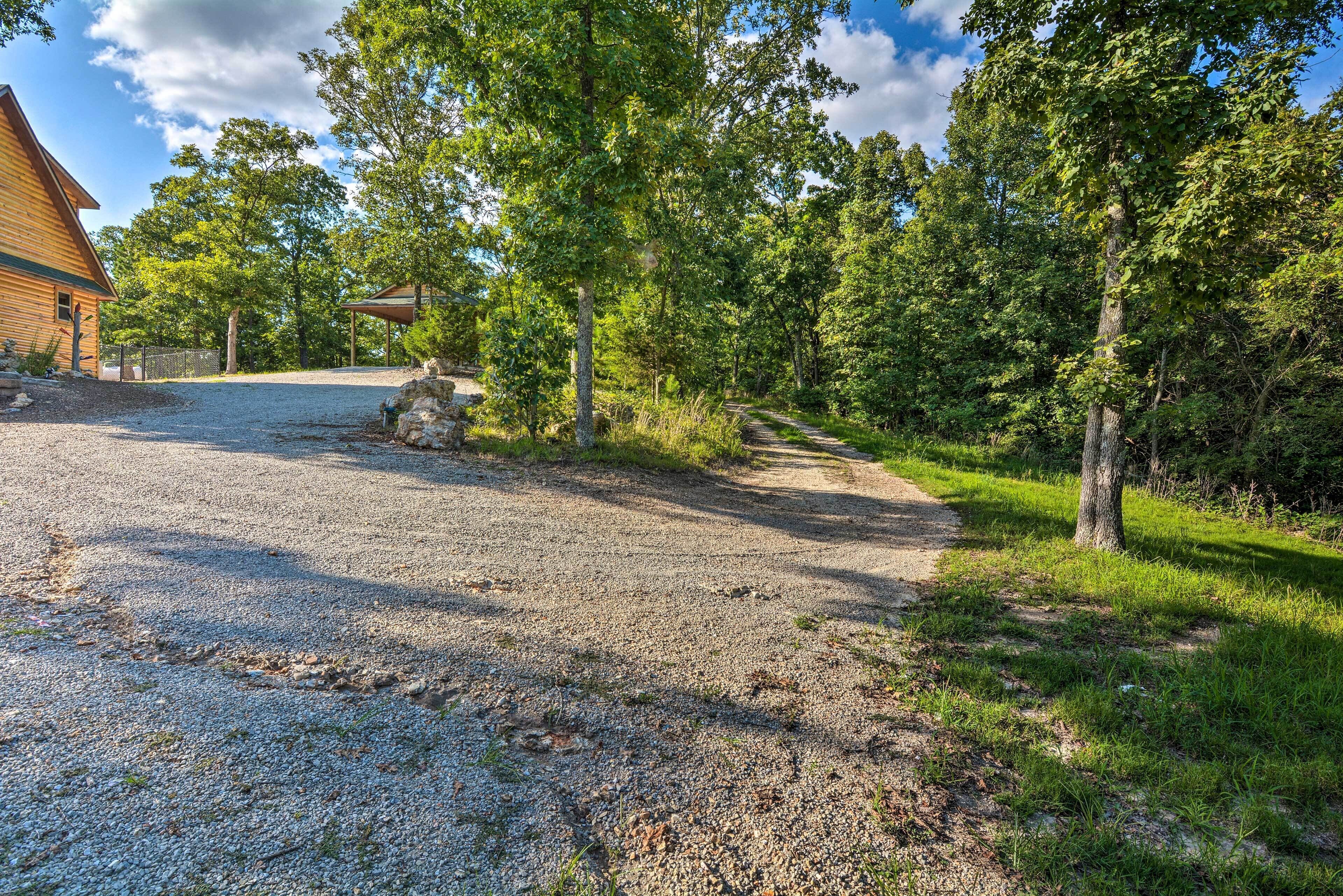 Un chemin de gravier mène à un chalet en bois doté d’un porche abrité, le tout entouré d’arbres touffus et d’une végétation luxuriante.