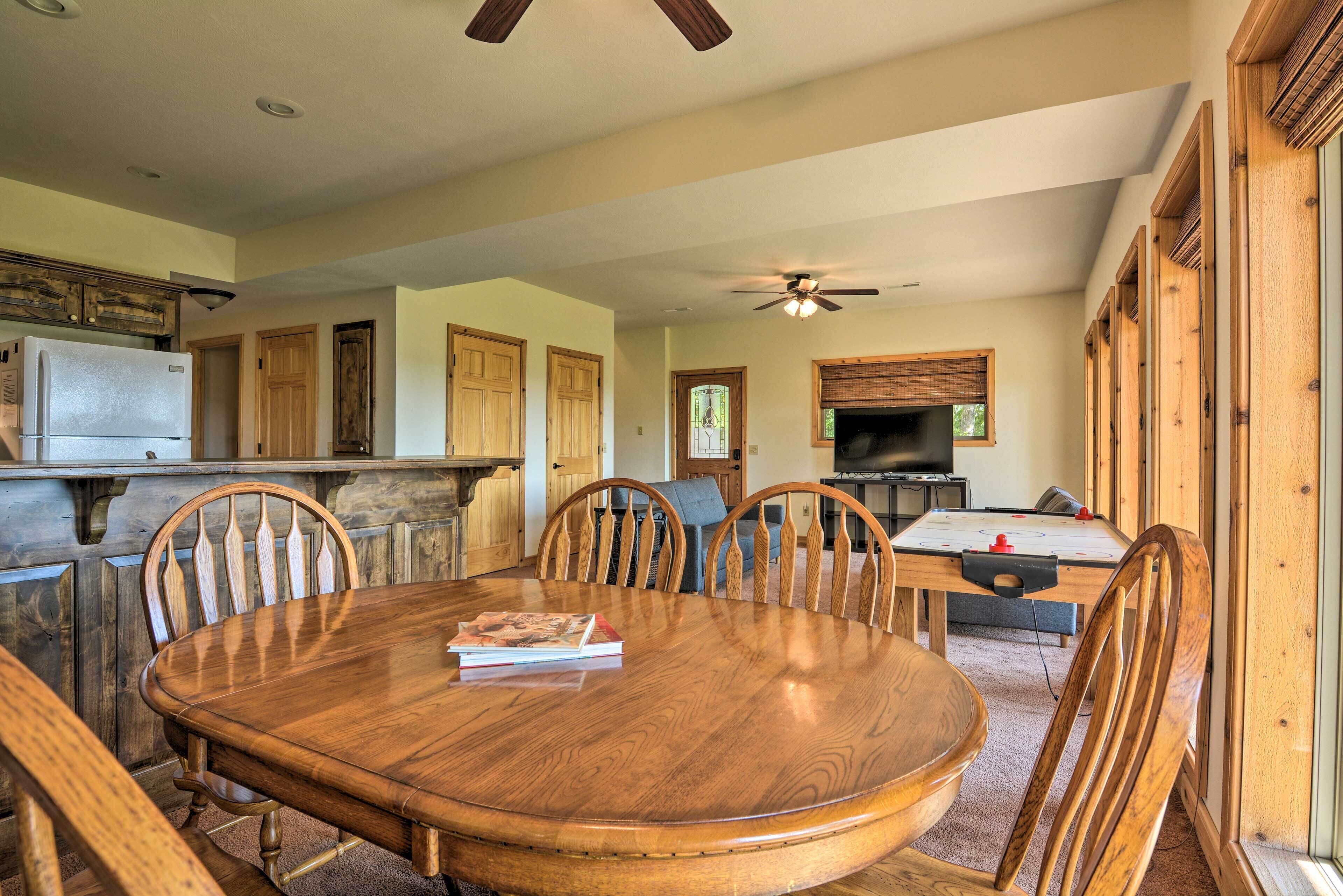 A spacious dining area with a wooden table and chairs, a built-in kitchen with a refrigerator, and a ceiling fan.