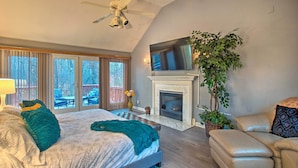A bedroom with a large bed, a fireplace, a TV mounted above it, and a balcony with outdoor furniture. - Lake Access, Hot Tub & 2 Decks: Ortonville Retreat (Ortonville)