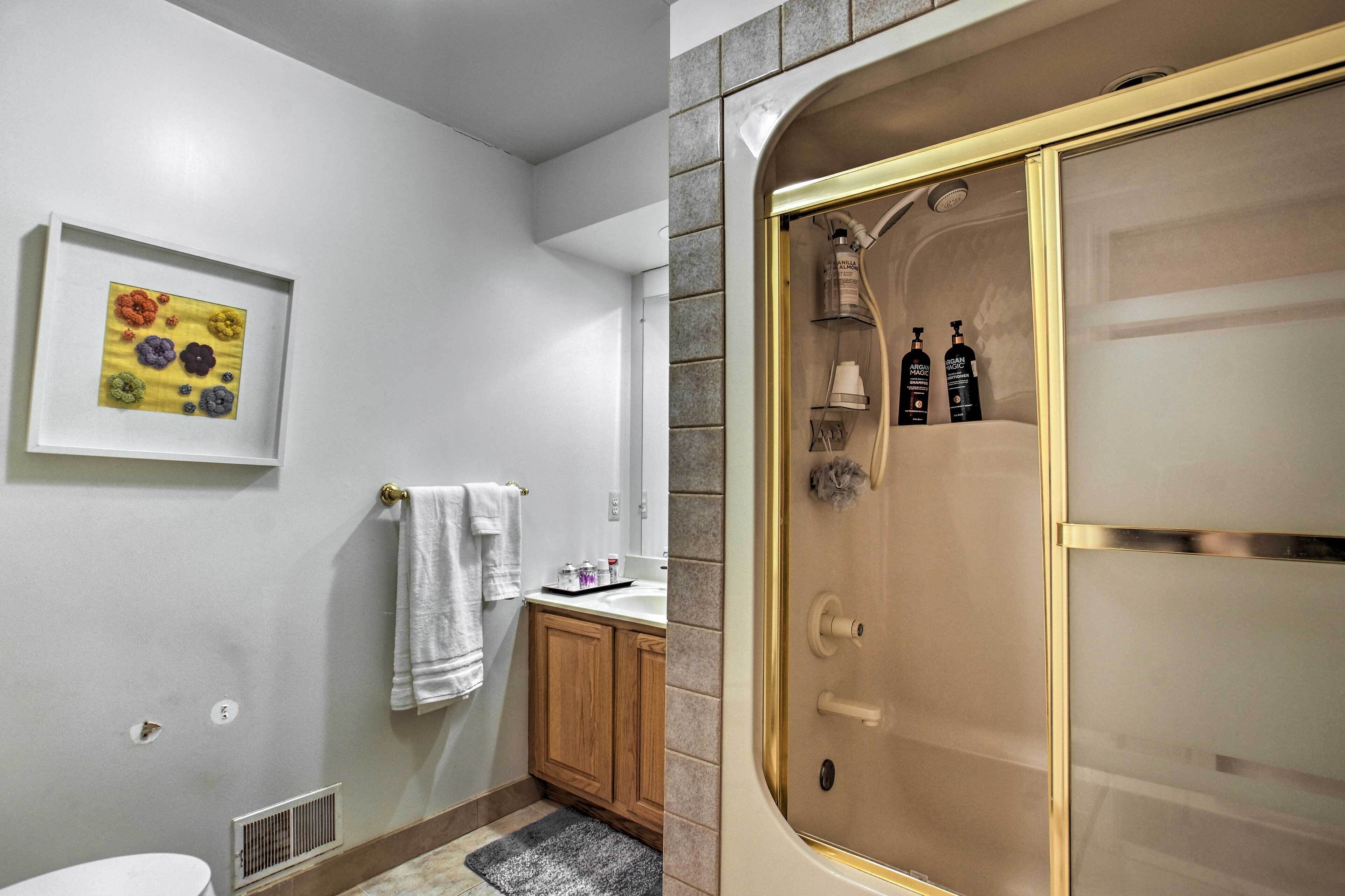 A bathroom with a shower, a sink, and a framed artwork on the wall.