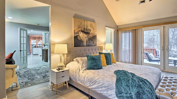 A bedroom with a large bed, a nightstand, a lamp, a window with blinds, and a view of the outdoors. - Lake Access, Hot Tub & 2 Decks: Ortonville Retreat (Ortonville)