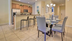 A modern kitchen with stainless steel appliances, a dining area with a glass table and gray chairs, and a chandelier. - Poolside Oasis in Paradise Palms: 6 Mi to Disney! (Kissimmee)