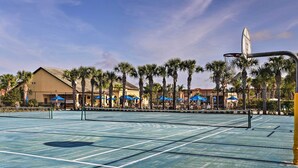 An outdoor tennis court with a net, surrounded by palm trees and buildings with blue awnings. - Poolside Oasis in Paradise Palms: 6 Mi to Disney! (Kissimmee)