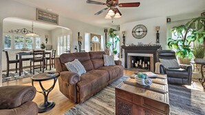 A spacious living room with a brown leather sofa, a black leather armchair, and a wooden coffee table. A ceiling fan and a fireplace are visible in the background. - Walk to Ventura Beach: Comfy Home w/ Ocean Views (Ventura)