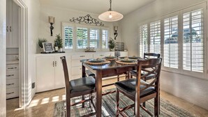 A dining area with a wooden table and chairs, a chandelier, and a view of the outdoors through large windows. - Walk to Ventura Beach: Comfy Home w/ Ocean Views (Ventura)