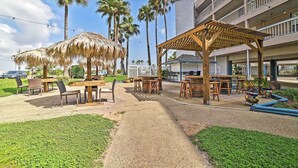 Un área de patio al aire libre con mesas y sillas de madera, un paraguas de paja y una pérgola.