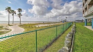 Un paseo marítimo con una cerca verde, palmeras y un edificio con balcones.