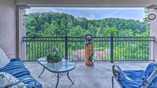 Un balcone con vista su una foresta, una scultura in legno e un tavolino in vetro con una pianta.