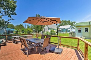 A wooden deck with a table and chairs, a large umbrella, and a view of houses in the background. - 'isle Have Another' - 1 Block to Colonial Beach! (Colonial Beach)