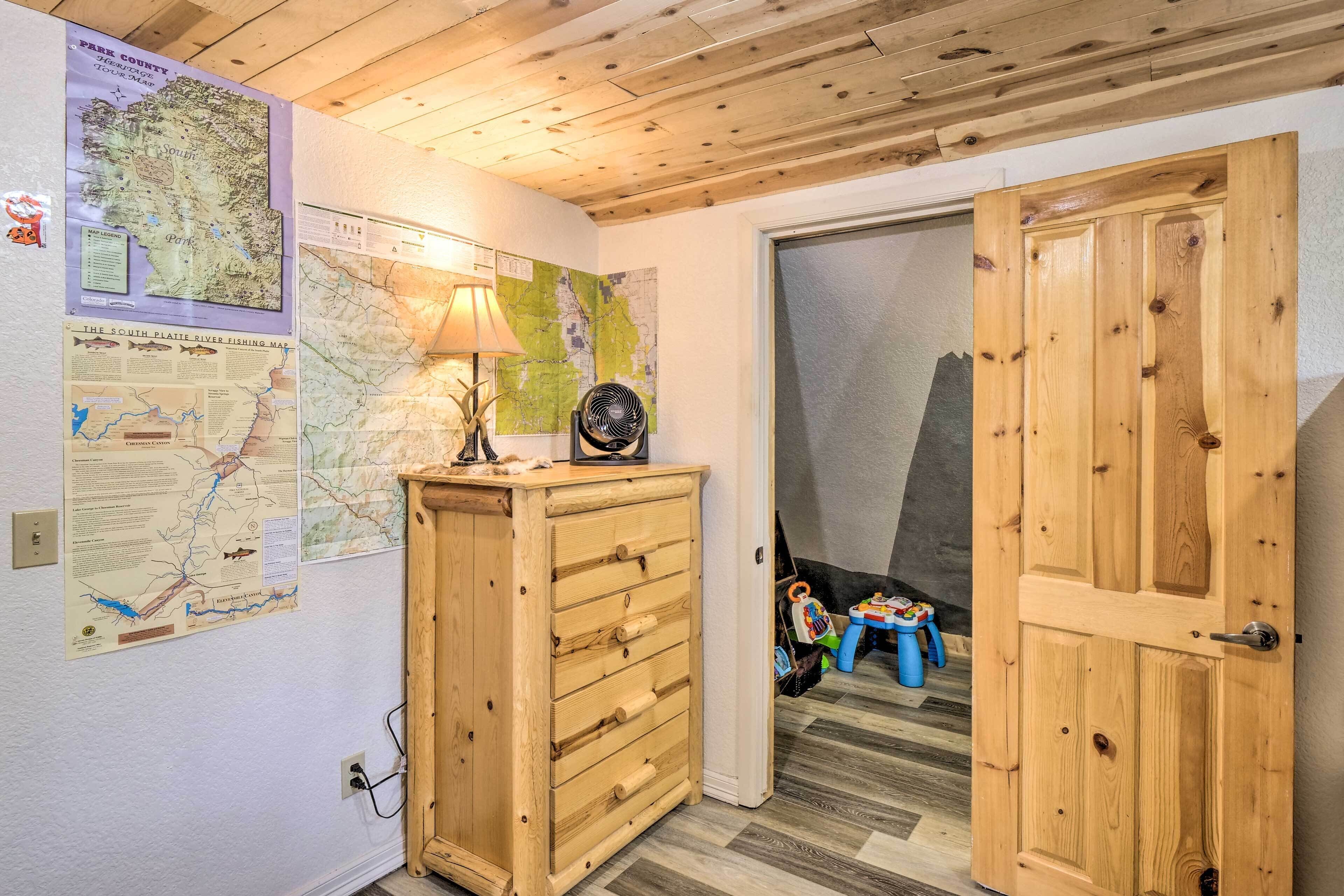 Una habitación con paredes y techo de madera, un aparador de madera, un mapa en la pared y una puerta que da a otra estancia.