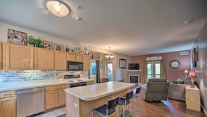 A modern kitchen with wooden cabinets, a central island with bar stools, and a dining area with a sofa and lamp. - Hunter Mountain Ski Retreat - Steps to Lift! (Hunter)