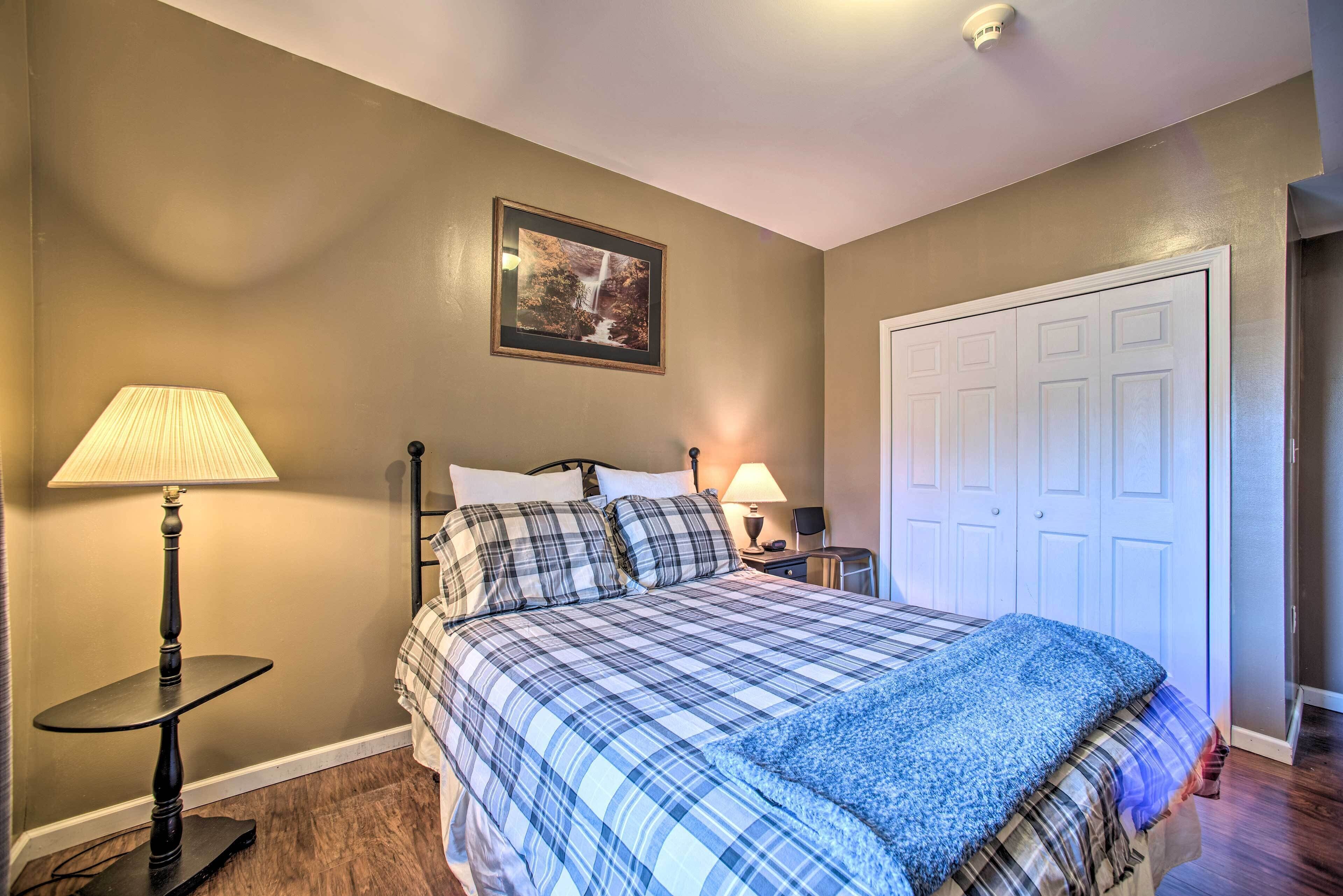 A bedroom with a bed, two bedside lamps, a framed picture on the wall, and a white door.