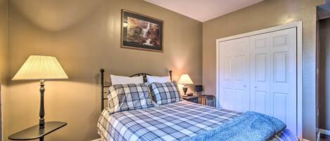 A bedroom with a bed, two bedside lamps, a framed picture on the wall, and a white door.