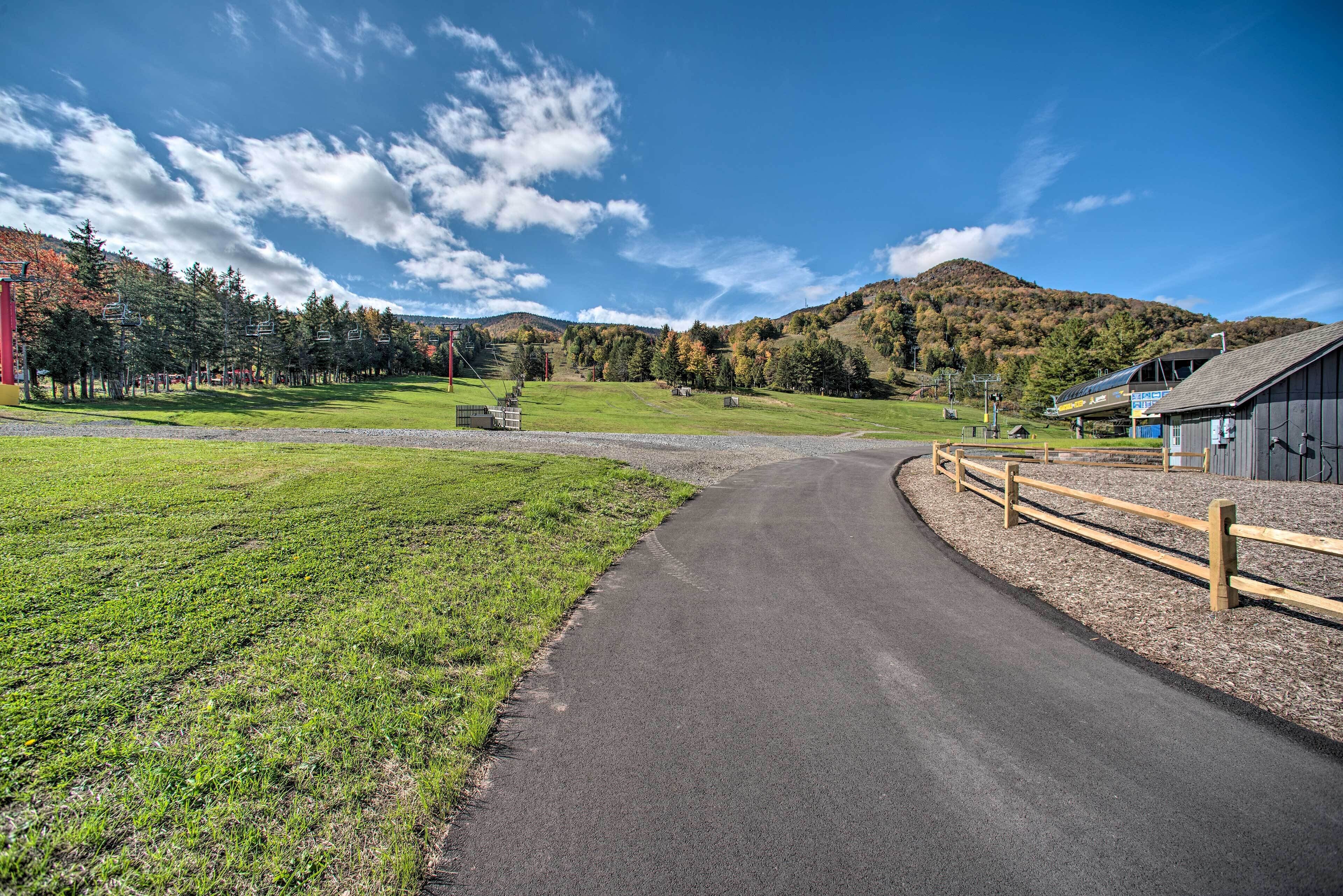 A rural road curving through a green field with a wooden fence on one side and a building on the other.