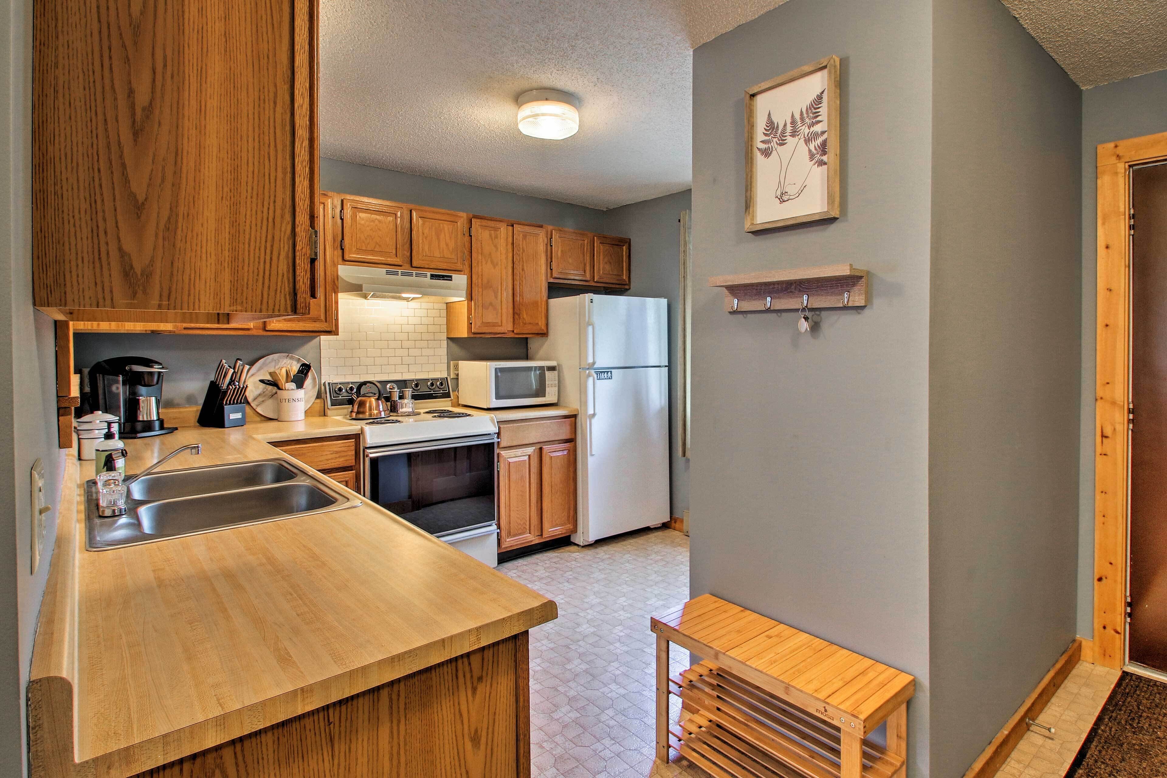 A compact kitchen with wooden cabinets, a stainless steel sink, a microwave, and a refrigerator.