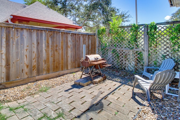 A backyard with a wooden fence, a barbecue grill, and a patio area with chairs.