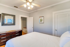 A bedroom with a bed, dresser, ceiling fan, and two doors.