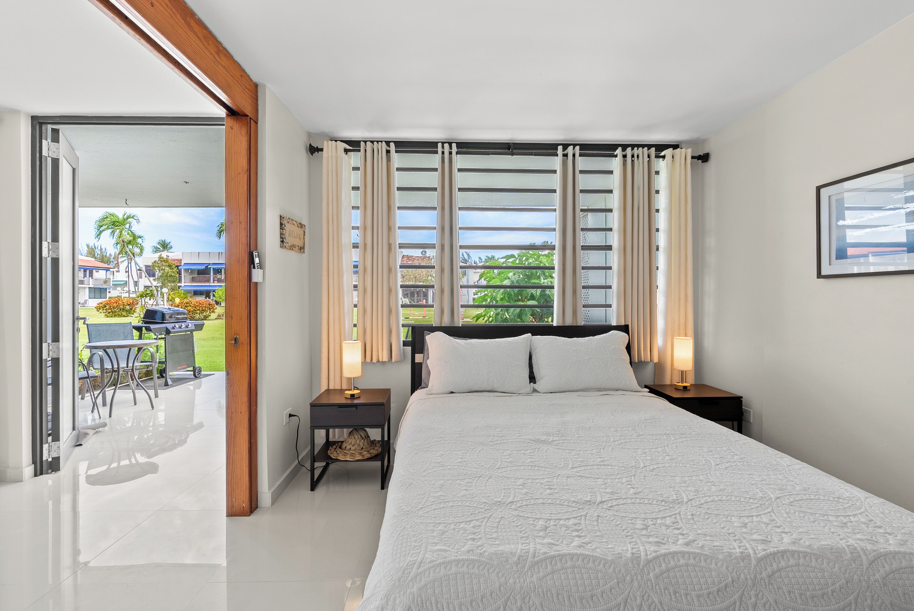 A bedroom with a bed, bedside tables, a window with curtains, and a view of the outside.