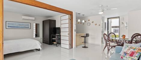 A modern living room with a sofa, a dining area with chairs, a kitchen area, and a bedroom with a bed.