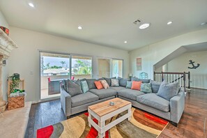 Ein modernes Wohnzimmer mit einem grauen Ecksofa, einem Holztisch und Blick ins Freie durch große Fenster.