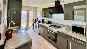 A modern kitchen with a central island, stainless steel appliances, and a sliding glass door leading to a patio.