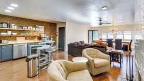 A modern kitchen with stainless steel appliances, a dining area with a table and chairs, and a living room with a sofa and two armchairs.