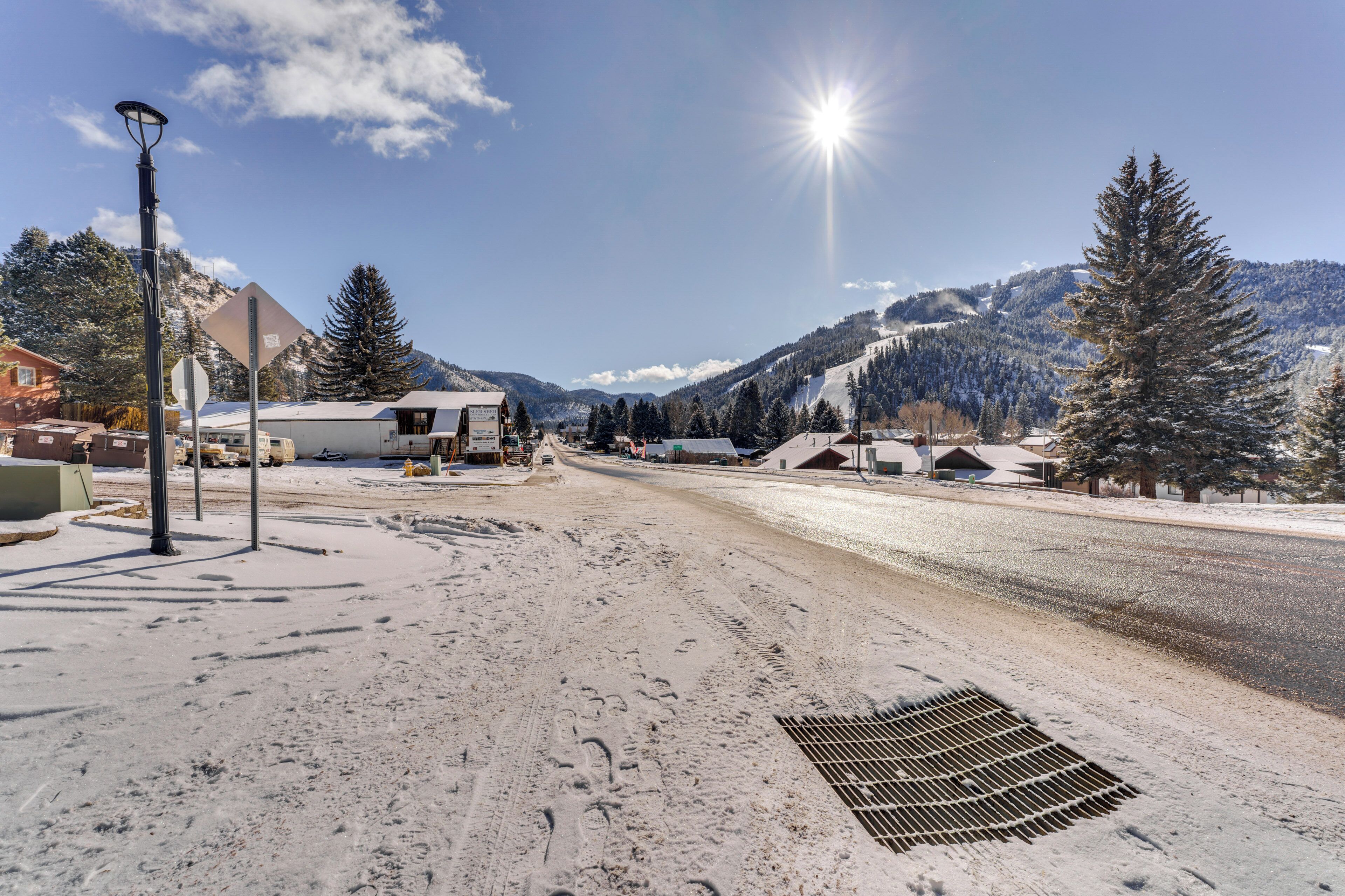 Une route enneigée avec une grille métallique, un lampadaire et des bâtiments en arrière-plan.