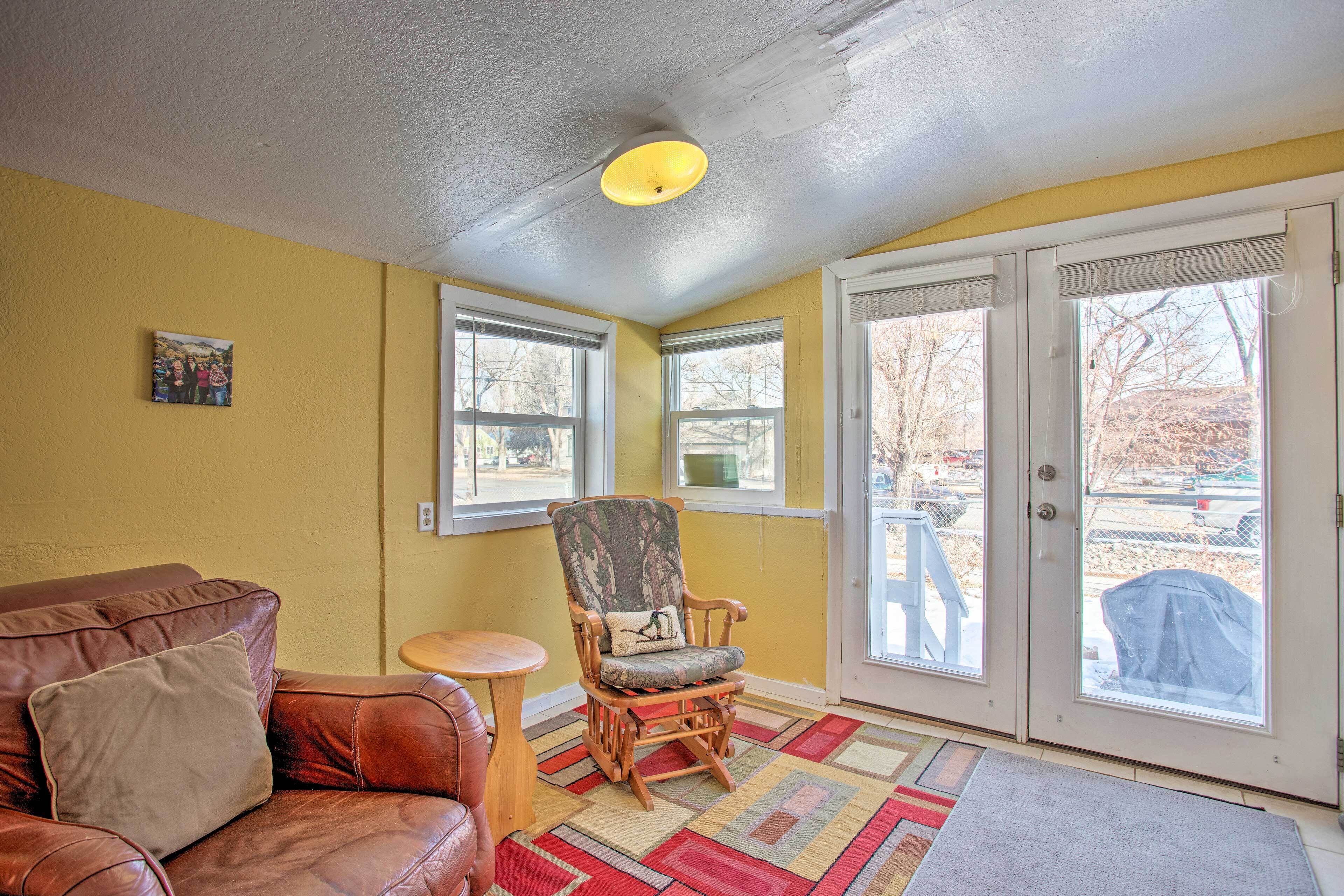 A room with a brown leather couch, a wooden rocking chair, a small round table, and a colorful rug.