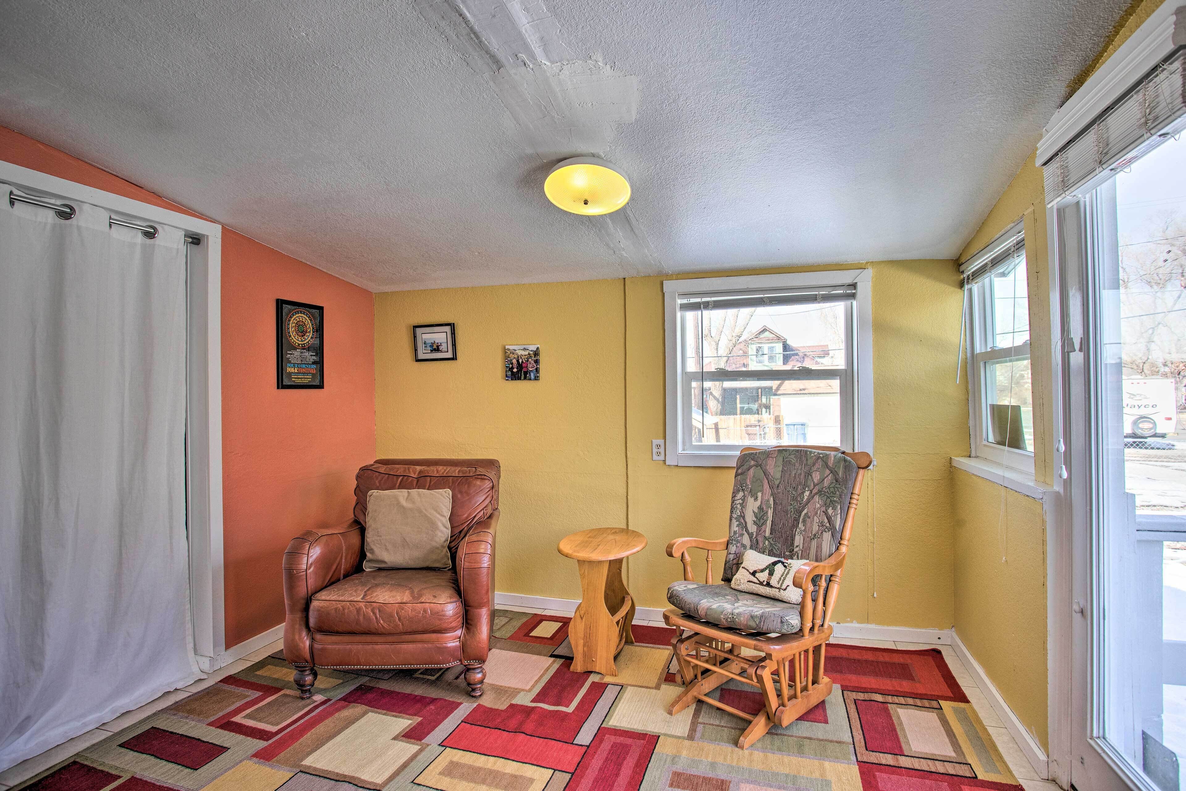 Une pièce comprenant un fauteuil en cuir marron, une chaise en bois, une petite table ronde et un tapis aux couleurs vives.